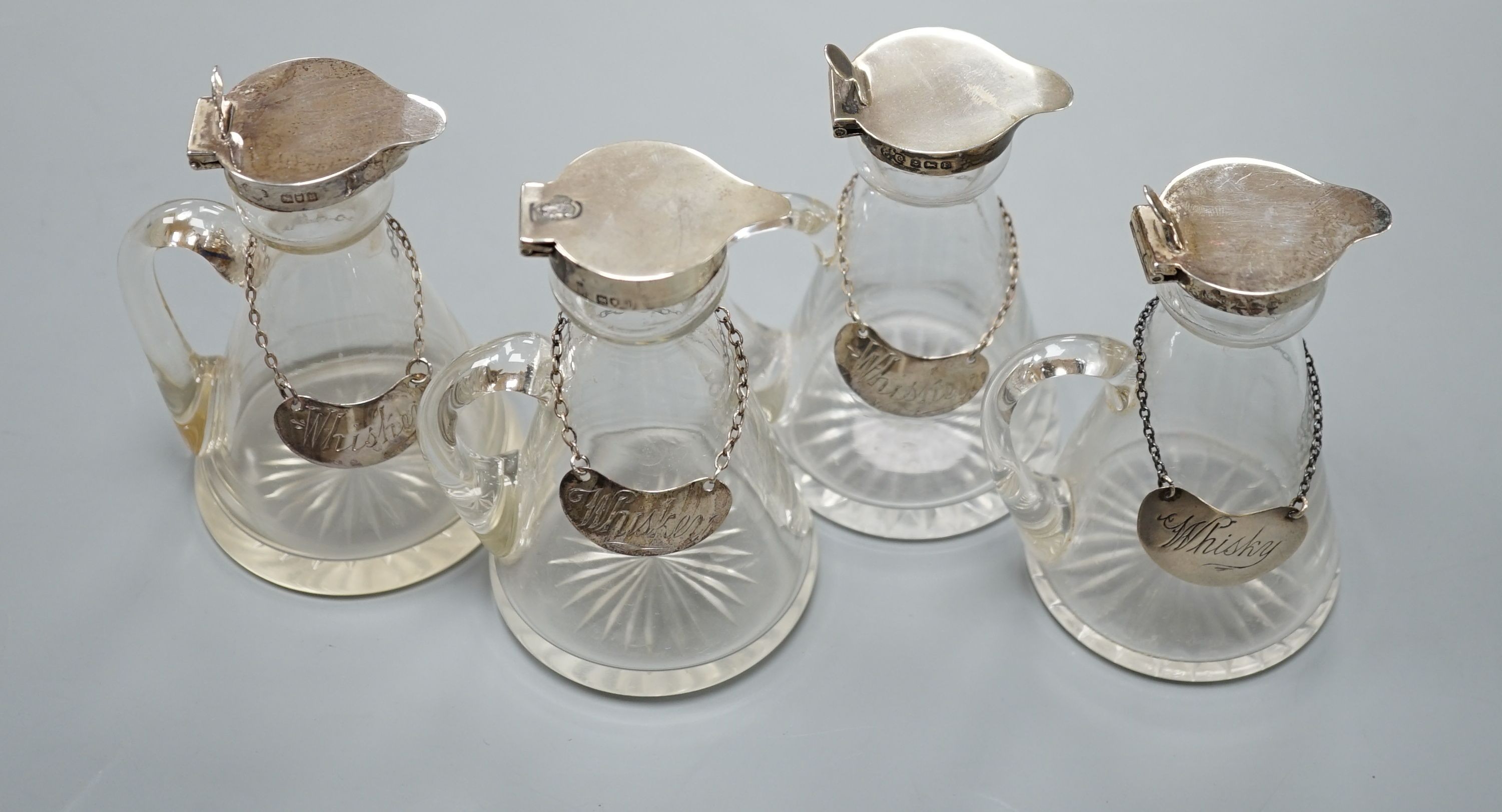 Four silver mounted cut glass whisky tots including a pair by Elkington & Co, 1930, 10.7cm, together with four assorted silver whiskey labels (one thumbpiece missing).